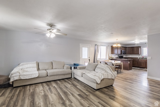 living room with ceiling fan with notable chandelier and dark hardwood / wood-style flooring