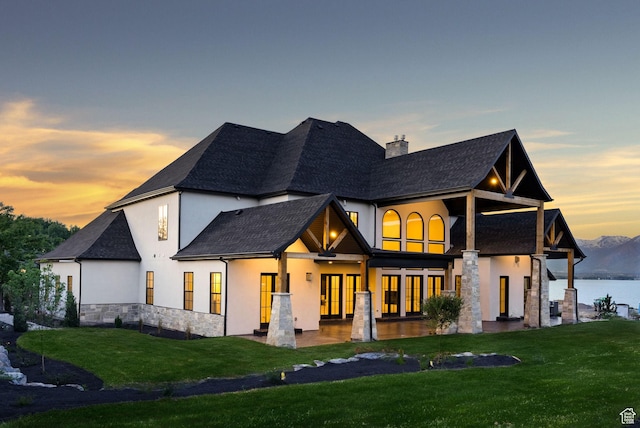 231 S Wiltshire Ln, Saratoga Springs, UT 84045 - back of house at dusk with stucco siding, stone siding, a yard, a chimney, and a shingled roof
