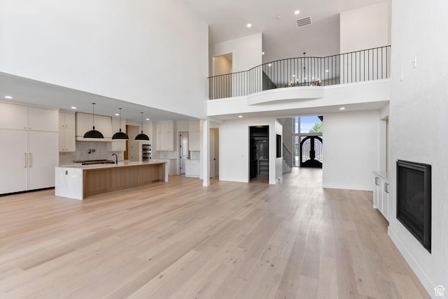231 S Wiltshire Ln, Saratoga Springs, UT 84045 - unfurnished living room with a glass covered fireplace, light wood-style floors, a towering ceiling, a sink, and recessed lighting
