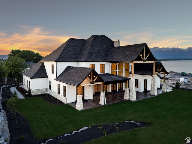 231 S Wiltshire Ln, Saratoga Springs, UT 84045 - back of house at dusk featuring stucco siding, a chimney, a lawn, and stone siding