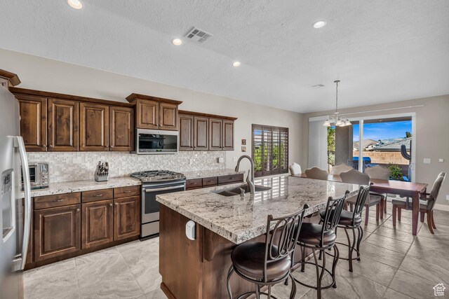3277 E 3180 S, St George, UT 84790 - kitchen with appliances with stainless steel finishes, a sink, decorative backsplash, a kitchen bar, and a center island with sink