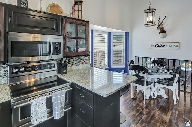kitchen featuring stainless steel appliances, light stone countertops, a notable chandelier, pendant lighting, and dark hardwood / wood-style flooring