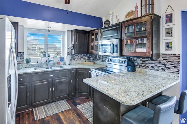 kitchen with dark hardwood / wood-style flooring, a textured ceiling, a breakfast bar area, backsplash, and appliances with stainless steel finishes