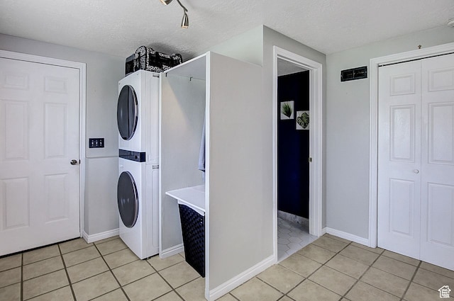 laundry area with a textured ceiling, stacked washer / dryer, and light tile patterned floors