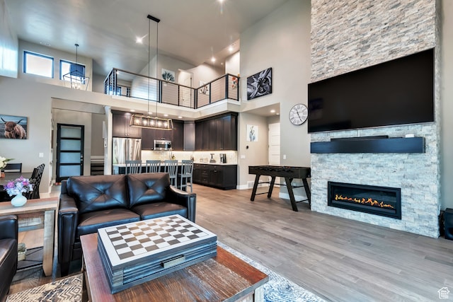 living room with a towering ceiling, a stone fireplace, light hardwood / wood-style floors, and a notable chandelier