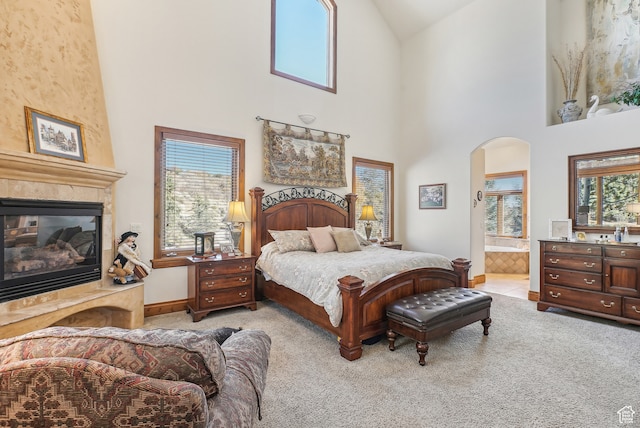 bedroom featuring ensuite bath, light carpet, a fireplace, and high vaulted ceiling