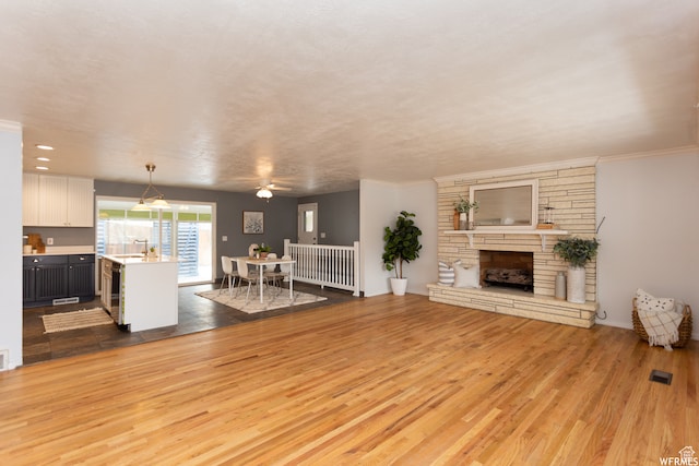 unfurnished living room with a fireplace, light hardwood / wood-style floors, ceiling fan, and crown molding