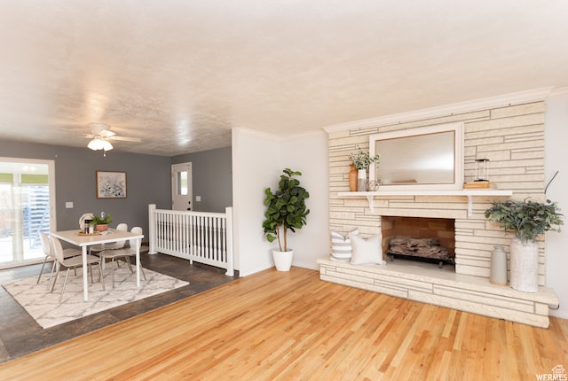 living room featuring a stone fireplace, hardwood / wood-style floors, ceiling fan, and crown molding