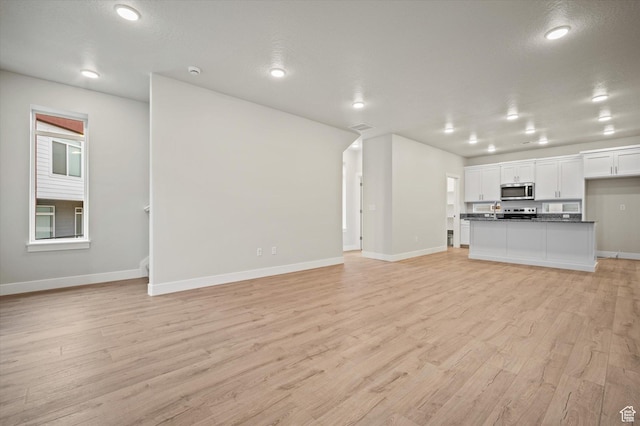 unfurnished living room with recessed lighting, visible vents, light wood-style flooring, a textured ceiling, and baseboards