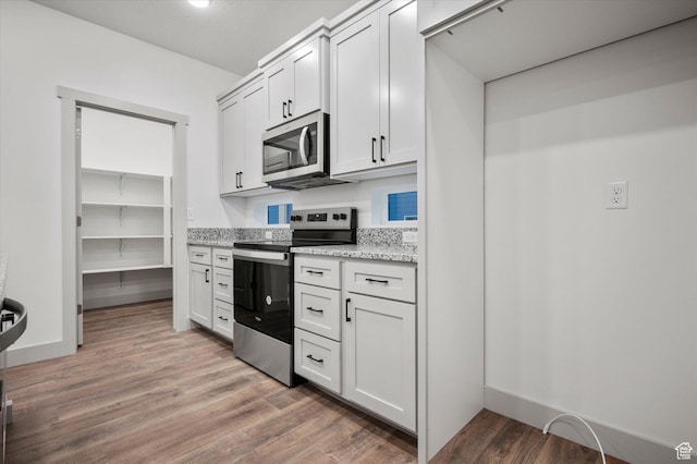 kitchen with light wood-style flooring, baseboards, white cabinets, appliances with stainless steel finishes, and light stone countertops