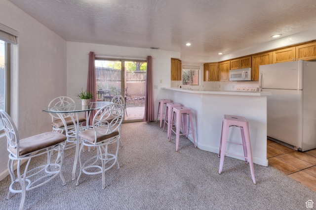 385 E Pueblo Ct, Moab, UT 84532 - kitchen featuring a textured ceiling, light carpet, white appliances, a kitchen bar, and kitchen peninsula