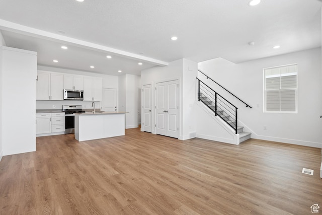 1084 E 1930 S Unit 423, Heber City, UT 84032 - kitchen with light hardwood / wood-style flooring, appliances with stainless steel finishes, white cabinetry, a center island with sink, and beamed ceiling
