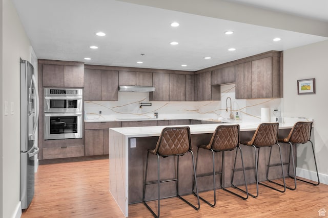 44 W Broadway S Unit 1205S, Salt Lake City, UT 84101 - kitchen with light wood-type flooring, kitchen peninsula, a breakfast bar, and stainless steel appliances