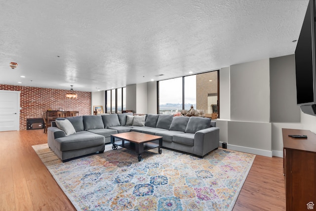 living room featuring a textured ceiling, brick wall, light hardwood / wood-style flooring, and floor to ceiling windows