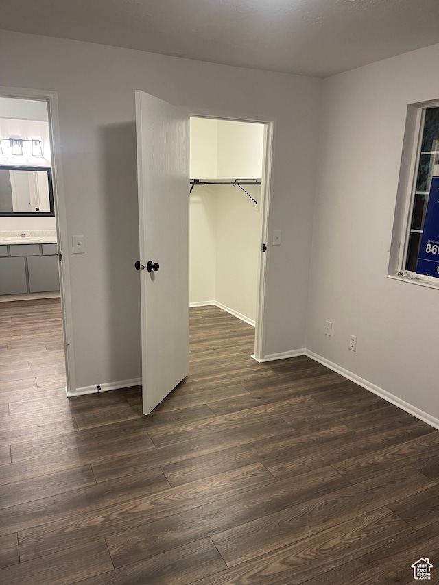 unfurnished bedroom featuring ensuite bath, dark hardwood / wood-style flooring, a spacious closet, and a closet