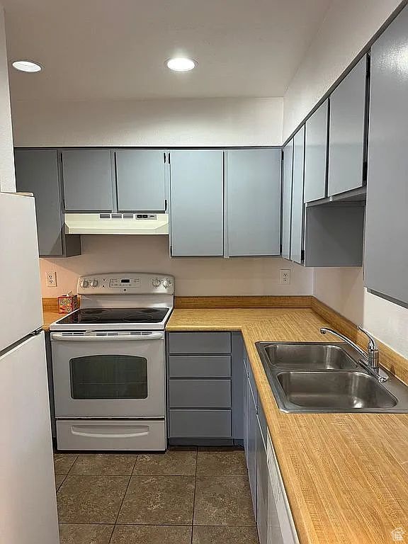 kitchen with dark tile patterned flooring, white appliances, and sink