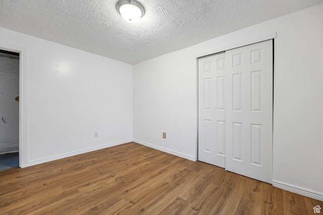 unfurnished bedroom with wood-type flooring, a textured ceiling, and a closet