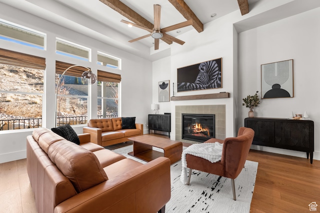 living room with ceiling fan, a tile fireplace, light wood-type flooring, and beam ceiling