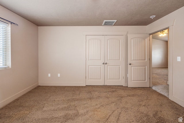 unfurnished bedroom featuring carpet flooring, a textured ceiling, a closet, and multiple windows