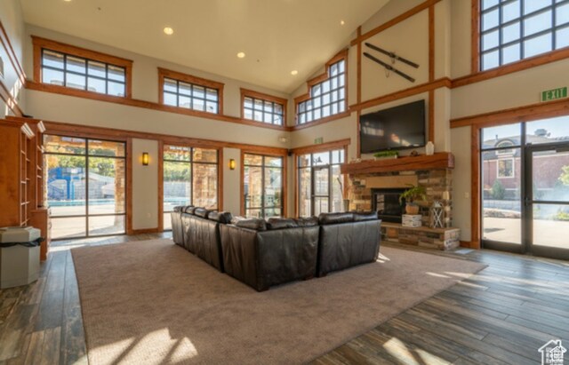 living room featuring wood finished floors, high vaulted ceiling, a stone fireplace, and a healthy amount of sunlight