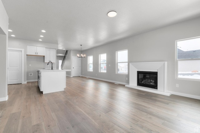 unfurnished living room featuring sink, a textured ceiling, an inviting chandelier, and light hardwood / wood-style flooring