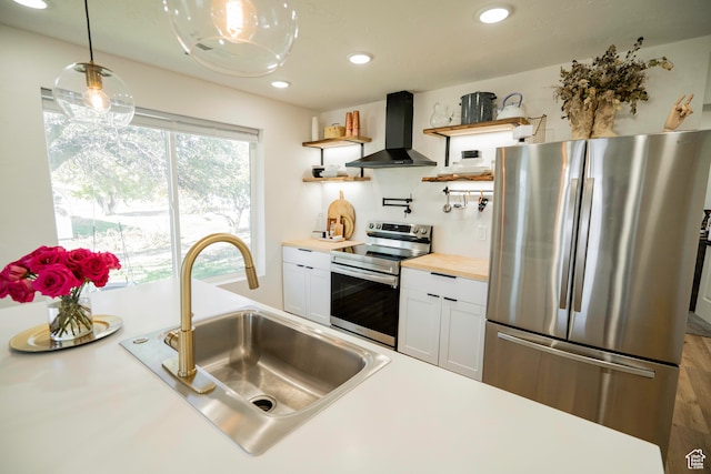 kitchen with pendant lighting, white cabinets, sink, range hood, and appliances with stainless steel finishes