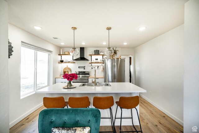 kitchen featuring hanging light fixtures, wall chimney exhaust hood, stainless steel appliances, and light wood-type flooring