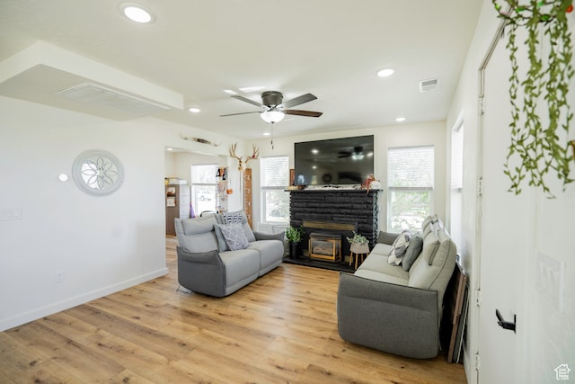living room featuring ceiling fan, a healthy amount of sunlight, a stone fireplace, and light hardwood / wood-style flooring