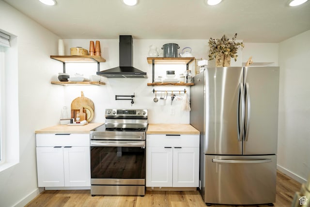 kitchen featuring wall chimney range hood, butcher block countertops, light hardwood / wood-style floors, white cabinets, and appliances with stainless steel finishes