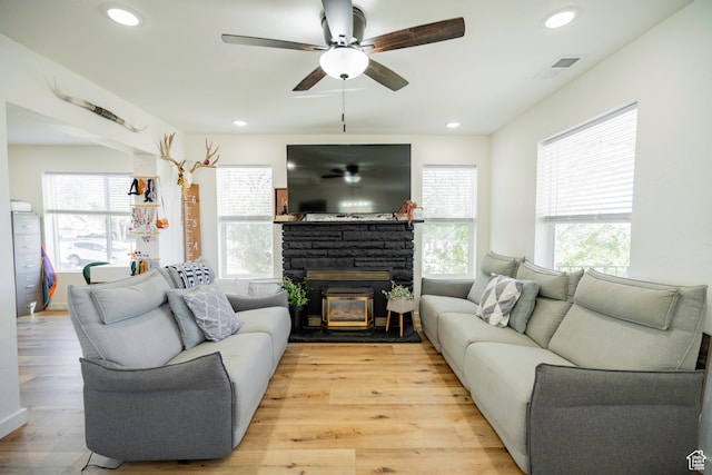 living room featuring a stone fireplace, a wealth of natural light, ceiling fan, and light wood-type flooring