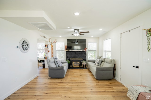 living room with light wood-type flooring, a stone fireplace, and ceiling fan