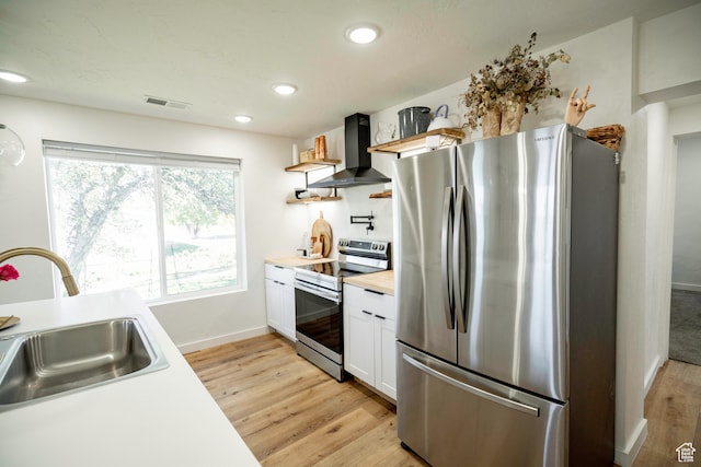 kitchen with white cabinets, wall chimney range hood, sink, appliances with stainless steel finishes, and light hardwood / wood-style floors