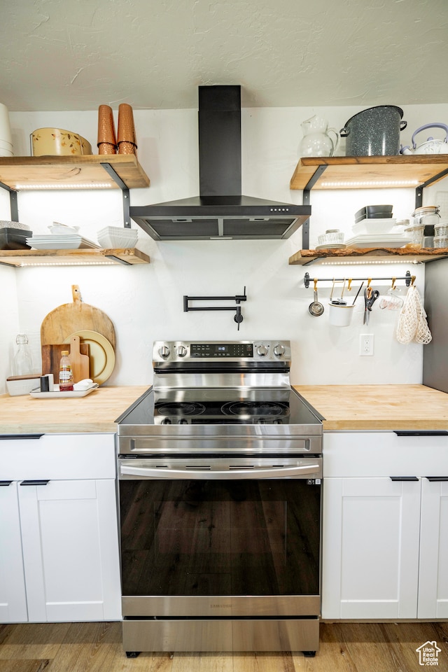 kitchen featuring stainless steel range with electric stovetop, wood counters, white cabinets, light wood-type flooring, and range hood