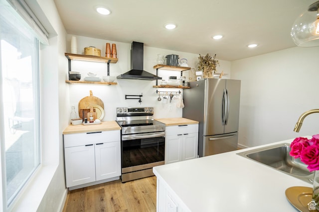 kitchen featuring white cabinets, stainless steel appliances, wood counters, and wall chimney range hood