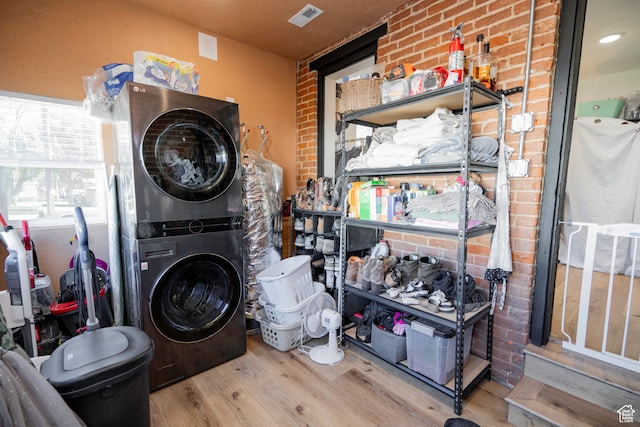 laundry area featuring brick wall, wood-type flooring, and stacked washer / drying machine