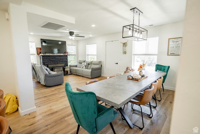 dining space featuring a fireplace, ceiling fan with notable chandelier, and light hardwood / wood-style flooring