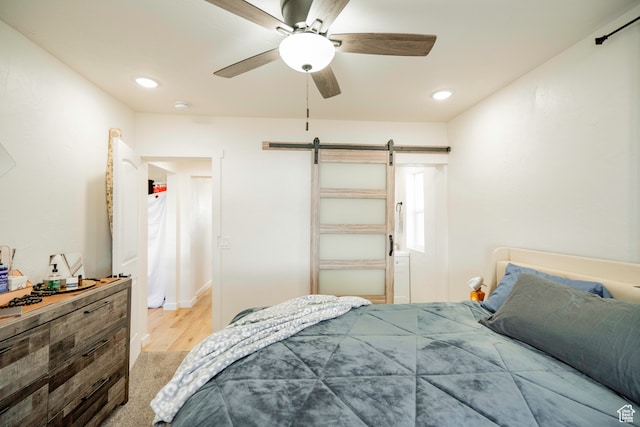 bedroom featuring a barn door, light hardwood / wood-style flooring, and ceiling fan