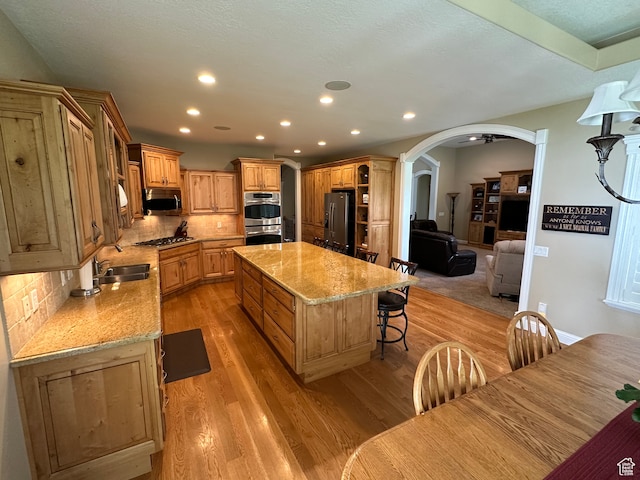 kitchen featuring a sink, appliances with stainless steel finishes, a center island, light wood-style flooring, and arched walkways