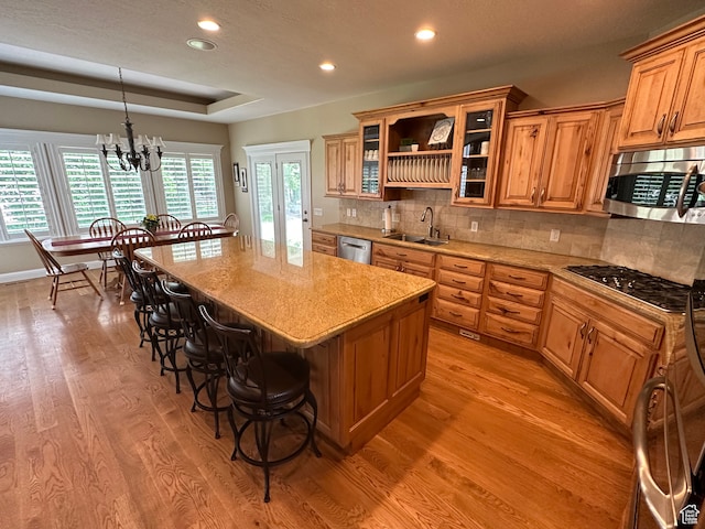 kitchen featuring appliances with stainless steel finishes, a sink, light wood-type flooring, a breakfast bar area, and a tray ceiling