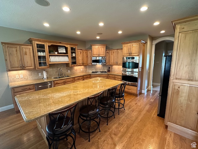 kitchen with a sink, a kitchen breakfast bar, light wood-type flooring, stainless steel appliances, and arched walkways