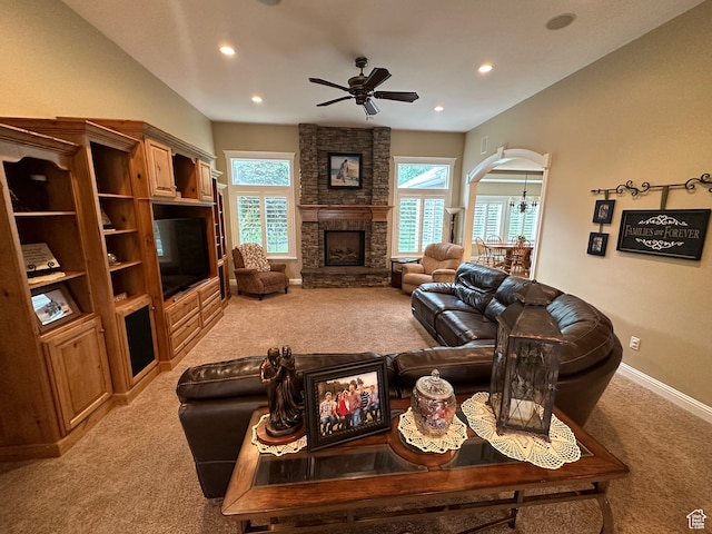 living room featuring baseboards, a stone fireplace, arched walkways, ceiling fan with notable chandelier, and light colored carpet
