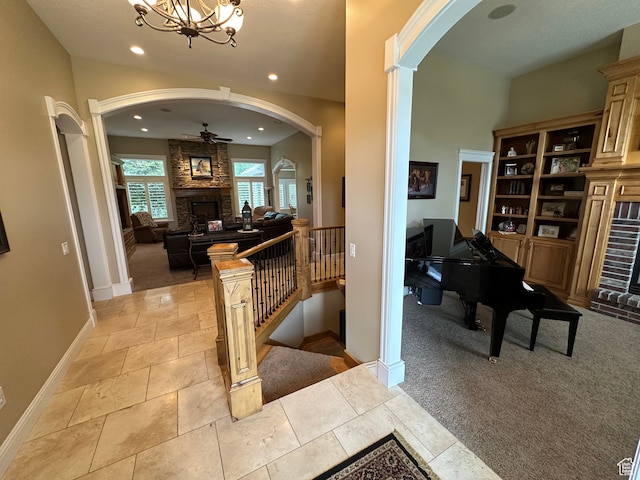 interior space with arched walkways, light colored carpet, a ceiling fan, and a stone fireplace
