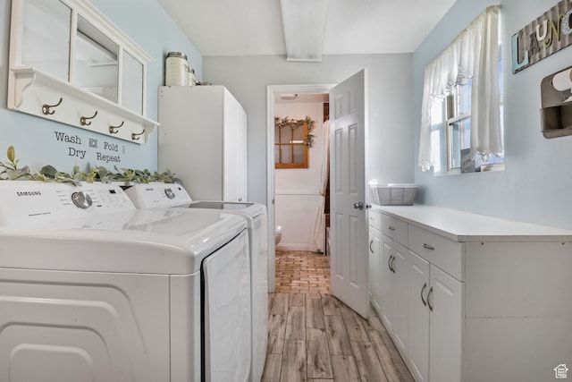 clothes washing area featuring cabinet space, light wood-style flooring, and separate washer and dryer