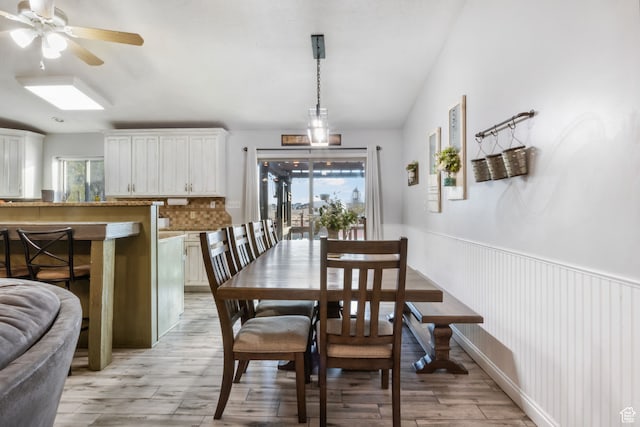 dining area with ceiling fan, vaulted ceiling, wainscoting, and light wood finished floors