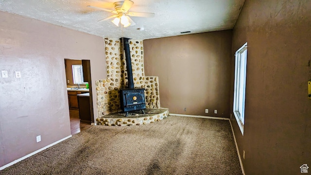 18250 N 4400 W, Fielding, UT 84311 - unfurnished living room featuring a wood stove, ceiling fan, carpet floors, baseboards, and a sink