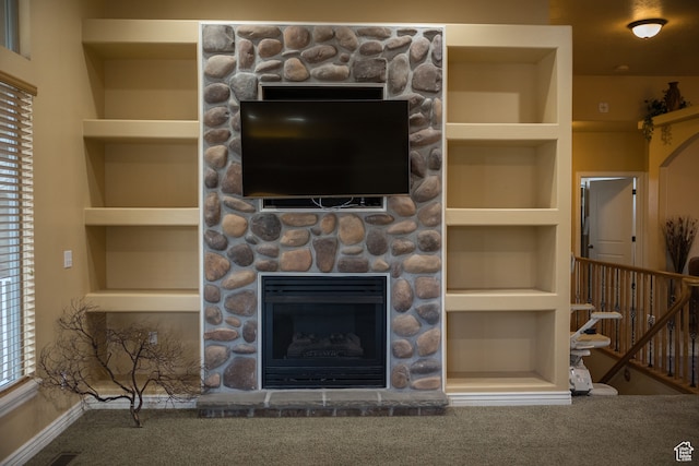 unfurnished living room featuring built in shelves, carpet floors, and a stone fireplace