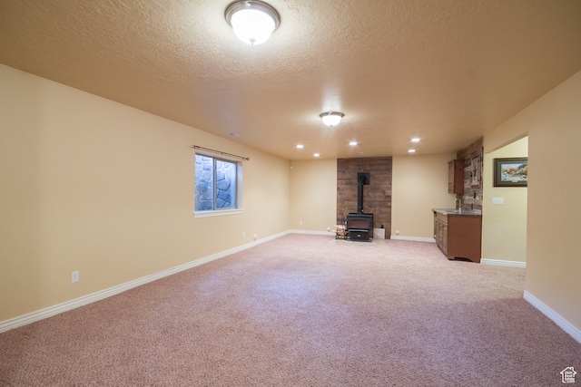 unfurnished living room with a wood stove, light carpet, and a textured ceiling