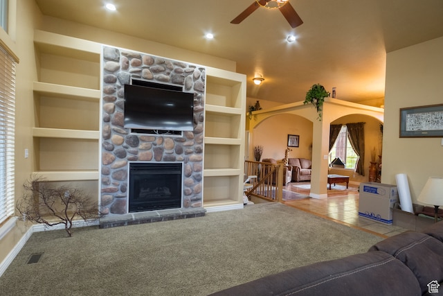 living room featuring built in shelves, ceiling fan, a fireplace, and carpet floors