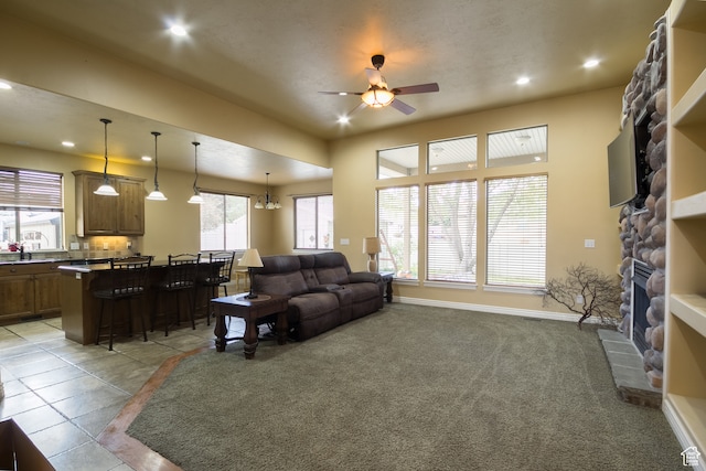 tiled living room featuring a stone fireplace, sink, and ceiling fan with notable chandelier