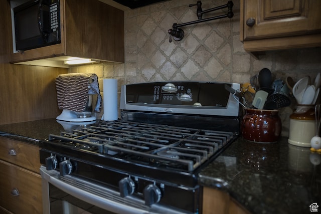 kitchen with stainless steel gas stove, dark stone countertops, and tasteful backsplash